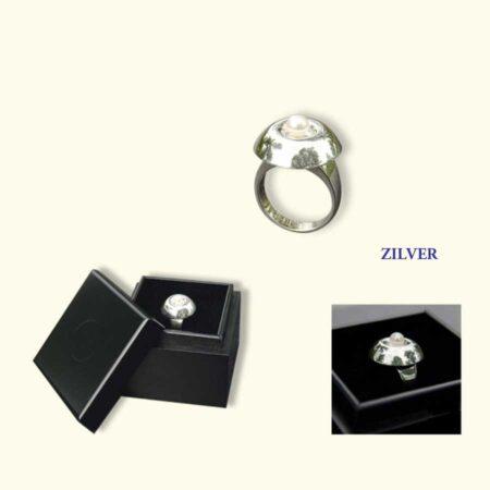 As-Cabochon van zilver, afgewerkt met een parel, op een ring. Hieronder is ruimte voor een wat as, wat aarde of een haarlokje.